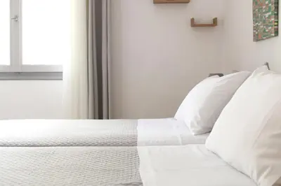 a white bed with white pillows and a cross on the wall at Ostria Rooms in Palaiochóra