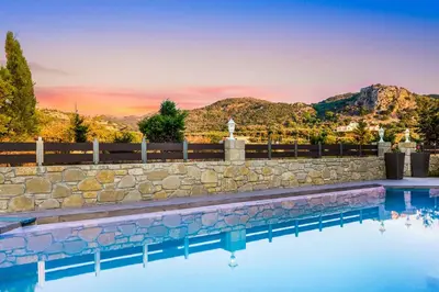 a swimming pool with a stone wall and mountains in the background at Villa Elenitsa in Nopíyia