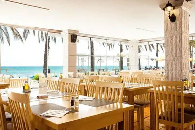 a restaurant with tables and chairs and the ocean at Alexandra Beach Hotel in Agia Marina Nea Kydonias