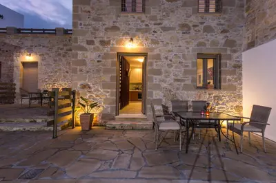 a patio with a table and chairs in front of a stone wall at Agarathos Deluxe Homes In the Heart of Kaliviani Near Balos in Kissamos