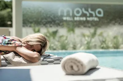 a young girl laying on a table next to a swimming pool at Mossa Well Being Hotel - Heated pool and Wellness Spa in Kato Daratso