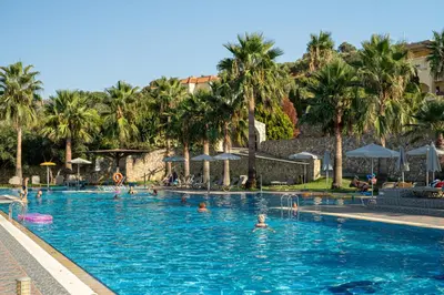 a swimming pool with palm trees and people in it at Almyrida Village & Waterpark in Almirida