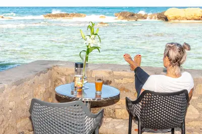 a woman sitting at a table looking at the ocean at Endless Blue Suites in Chania Town