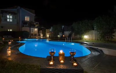 a swimming pool at night with candles and wine glasses at Ifigeneia's Lavish Escape with Private Hot Tub in Kalathas