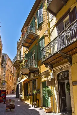 a yellow building with balconies and tables on a street at Antica Casa Studios in Chania Town