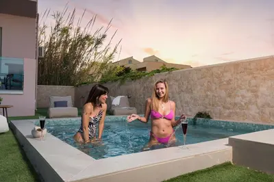 two women in bathing suits in a swimming pool at Aegean Breeze Luxury Apartments next to the sea in Maleme