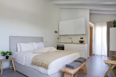 a white bedroom with a large bed and a kitchen at s u e ñ o - studios and apartments, with shared pool in Kato Daratso