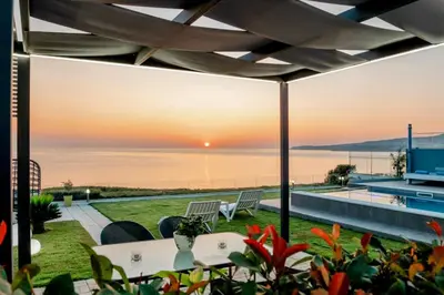 a patio with a view of the ocean at sunset at Blue Green Villa Kalyves eco pool premium quality in Kalyves