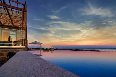 a building with a swimming pool next to the ocean at Athinais villa in Palaiochóra