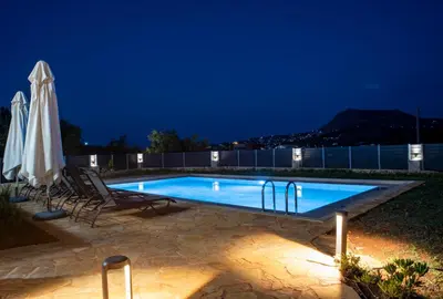 a swimming pool at night with chairs and an umbrella at Horizon Villa Almyrida in Almirida