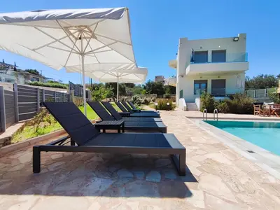 a group of lounge chairs with an umbrella next to a swimming pool at Horizon Villa Almyrida in Almirida