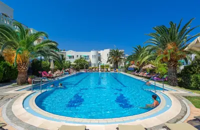 a large pool with palm trees and people in it at Castle Suites Hotel in Plataniás