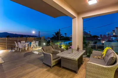 a patio with chairs and a table on a deck at night at Luxury Villa Crete Villa Marina Mare 3 Bedroom Private Pool in Chania Town