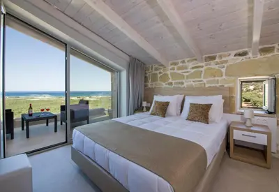 a bedroom with a large bed and large windows at Petras Resort in Falasarna