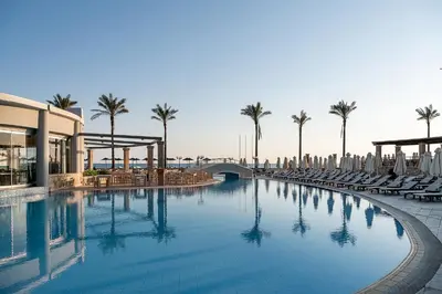 a large swimming pool with chairs and palm trees at Caldera Beach in Plataniás