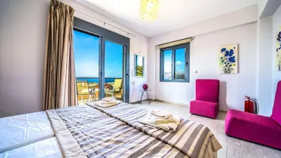 a bedroom with a large bed and two pink chairs at Anemon Villas in Kissamos