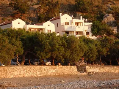 a large white house on a hill behind trees at Ravdoucha Beach Studios in Ravdhoúkha
