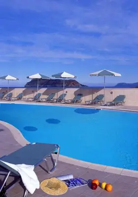 a blue swimming pool with chairs and umbrellas at Lissos Beach in Plataniás