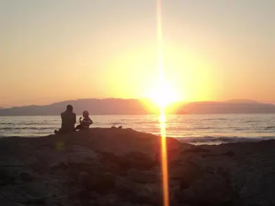 a man and a child sitting on the beach watching the sunset at Thodorou Village in Agia Marina Nea Kydonias