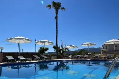 a swimming pool with chairs and umbrellas and a palm tree at Odos Oneiron Tavronitis Bay in Tavronitis