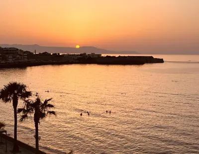 a beach with people swimming in the water at sunset at zonapartments A sea view-city center in Chania Town