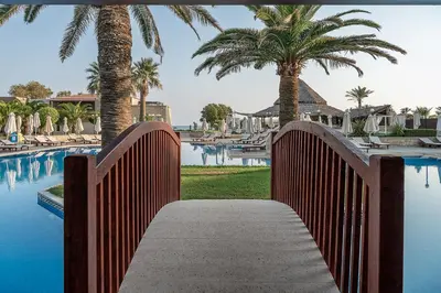 a wooden walkway leading to a swimming pool with palm trees at Caldera Creta Paradise in Plataniás