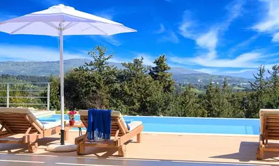 a patio with two chairs and an umbrella and a pool at Orientem Villa Heated Pool in Georgioupoli