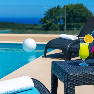 a drink on a table next to a swimming pool at Sea Breeze & Stunning Views - Pool Dream Gem in Dhémbla