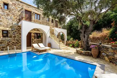 an outdoor swimming pool in front of a house at Minos Country Living Apartments in Agrilés