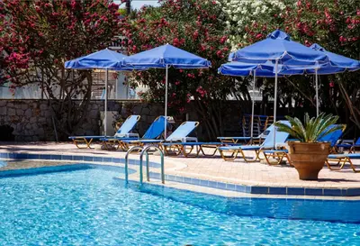 a swimming pool with blue umbrellas and lounge chairs and a swimming pool at Lili Apartments,oasis 2,5 km from Hania center in Parigoría