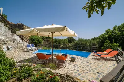 a patio with an umbrella and chairs and a pool at Villa Zoi Tzitzifes in Tzitzifés