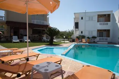 a swimming pool with chairs and an umbrella next to a building at Elena Rooms & Apartments in Gerani Chanion