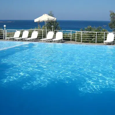 a large blue swimming pool with chairs and an umbrella at Hotel Plakures in Falasarna