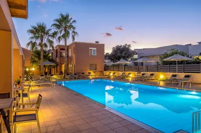 a pool at night with chairs and umbrellas at Theos Holidays Apartments in Kato Daratso