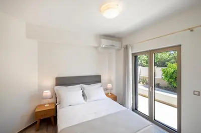 a white bedroom with a bed and a window at Villa Persephone in Tavronitis