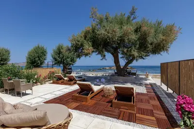 a patio with chairs and a tree and the ocean at Villa Seashell -Wonderful newly renovated villa on the beach in Galatás
