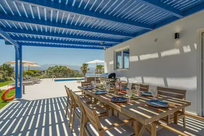 a wooden table on a patio with a blue ceiling at Villa Hemera ocean view private heated pool in Chorafakia