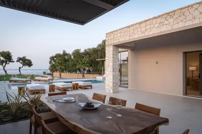 an outdoor dining area with a wooden table and chairs at Artemis Villa, Beachfront Retreat with Heated Pool, By ThinkVilla in Tavronitis