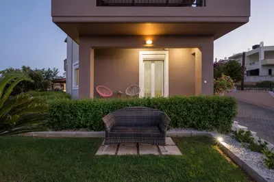 a wicker chair sitting in the grass in front of a house at Tholos Apartments in Chania Town