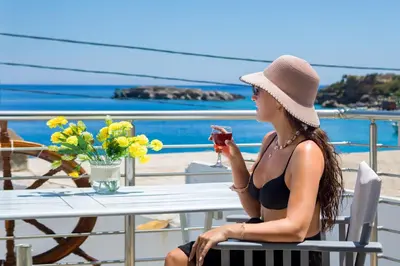 a woman in a hat sitting at a table with a drink at Plori - Molos Apartments in Loutro