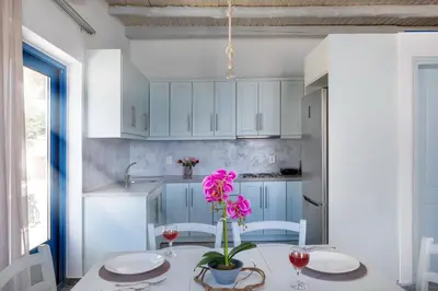 a kitchen with white cabinets and a table with pink flowers at Plori - Molos Apartments in Loutro