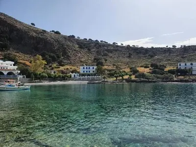 a boat in a body of water next to a mountain at EDEM HOUSE FINIKAS in Loutro