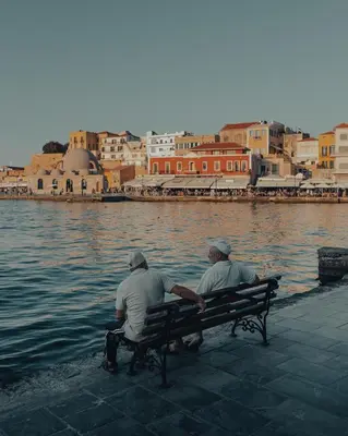 two men sitting on a bench next to the water at Thyme Sea View Apartments by 8essentially in Souda