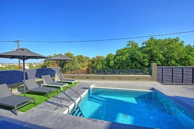 a swimming pool with two chairs and an umbrella at Villa Maripol by PosarelliVillas in Galatás