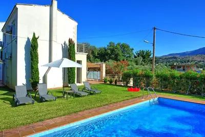 a swimming pool in a yard with chairs and an umbrella at Villa Politini by PosarelliVillas in Vryses
