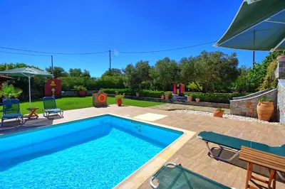 a swimming pool in a yard with chairs and an umbrella at Villa Antina by PosarelliVillas in Litsárdha