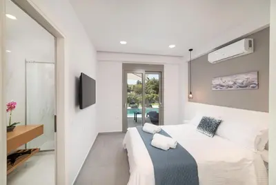 a white bedroom with a large bed and a tv at Villa Ampela by PosarelliVillas in Agia Marina Nea Kydonias