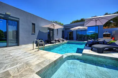 a swimming pool with chairs and umbrellas next to a house at Villa Zaneti by PosarelliVillas in Agia Marina Nea Kydonias