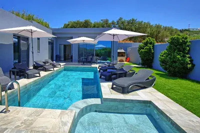a swimming pool with chairs and umbrellas next to a house at Villa Zaneti by PosarelliVillas in Agia Marina Nea Kydonias