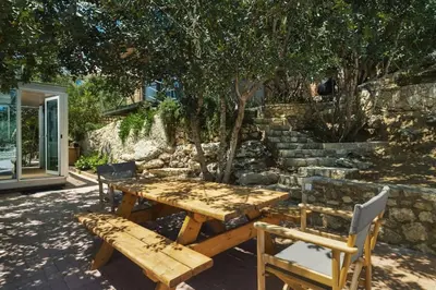 a wooden picnic table with two chairs and a stone wall at Luxury TreeHouse - A breath away from the beach in Loutrákion
